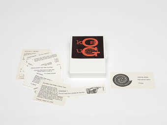 (.1) A white plastic box with a Maciunas designed label in black print against red background. ...