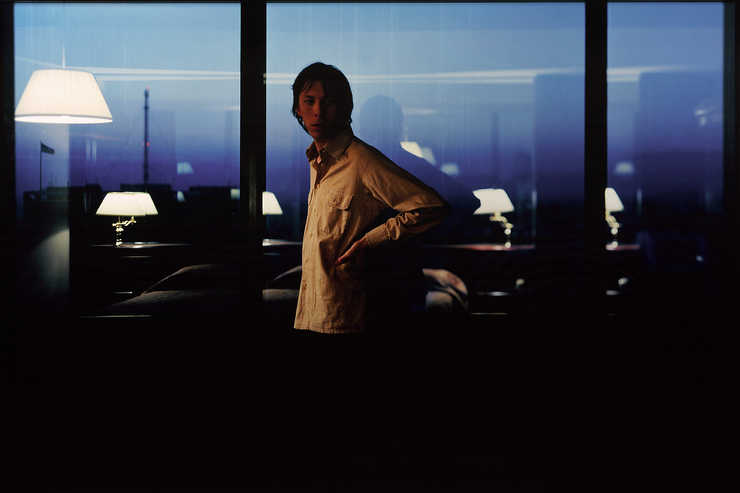 A man standing in front of a curtain wall of windows, reflected in the windows is the interior of...