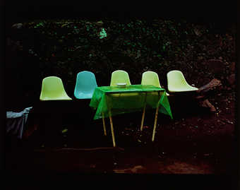 5 colorful chairs in a row before a table with a green tablecloth in an outdoor setting