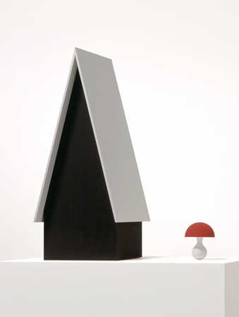 A black house with a white roof next to a red capped mushroom with a white stem.