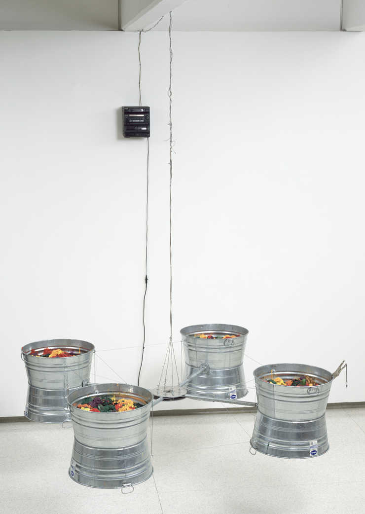 Four wash buckets fastened together with pipe and cable.  buckets are filled with colored...