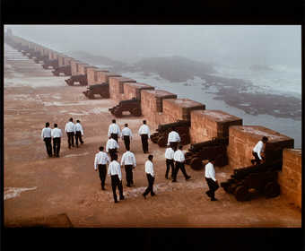 An image of men dressed in white shirts and black pants on the roof of a fortress in Morocco