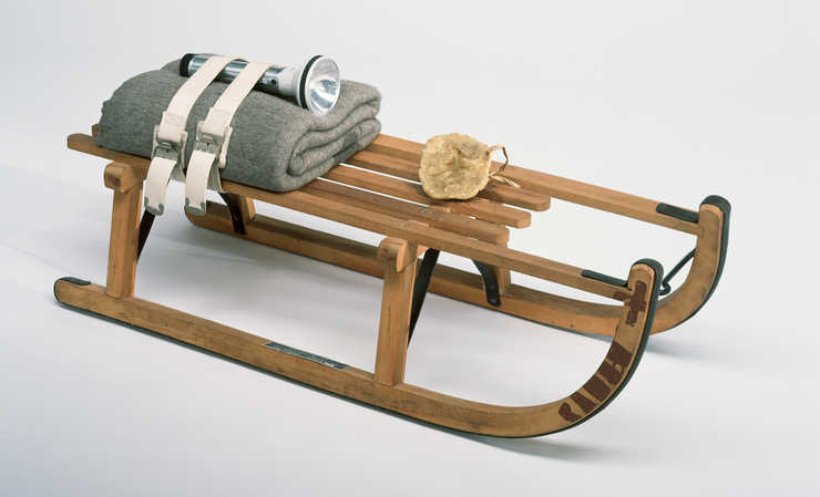 Wooden sled with metal runners and supports, lump of fat tied to top, and  folded felt blanket...