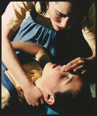 an image of twin girls  dressed identically.  One is about to give the other mouth to mouth...