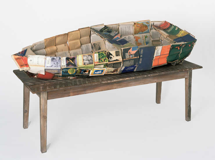 a boat constructed of a metal armature and composed of Cuban text books; boat rests on a wood table