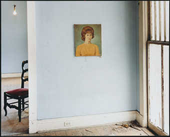 A image of the crumbling interior of an empty residence, with the exception of a painted portrait...