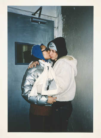 young man and woman kissing in doorway; woman is wearing a silver winter jacket