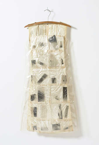 A white satin dress covered with vinyl and cellophane pockets that contain photographic...