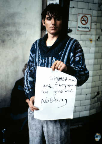 An image of a man holding a hand written sign that reads "I Signed On and They Would Not...