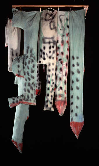 14 stufffed muslin buildings hang from rack, attached with clothespins and wire hangers