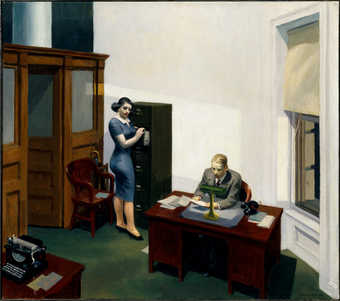 Interior of an office.  Man sitting behind a desk reading some papers which he holds with both...