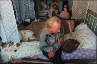 A slighlty out of focus image of the artist's father seated on a bed next to a dog, the...