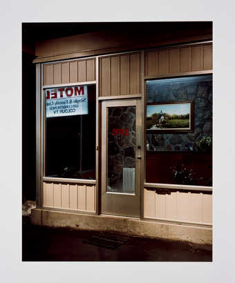 An image of the exterior of a motel lobby with the sign reflected in the window.