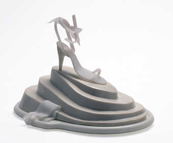 screenprinted videodisc; cream colored shoe with fabric bow on top of a stepped platform with...